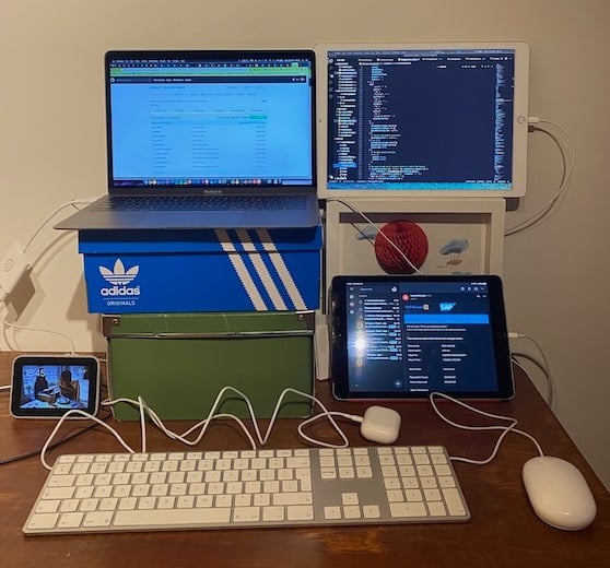 两把椅子放着一张学习长凳。学校长椅顶部放着鞋盒，可支撑一台笔记本电脑和周围放着两台 iPad。